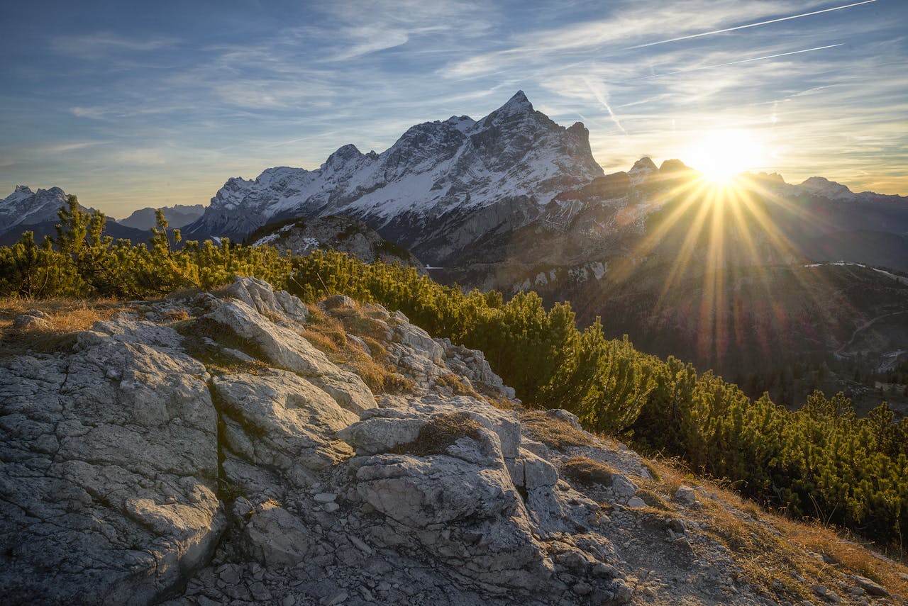 our-story Stunning sunrise casting rays over the Italian Alps in Alleghe, Veneto, with lush greenery and rocky terrain.
